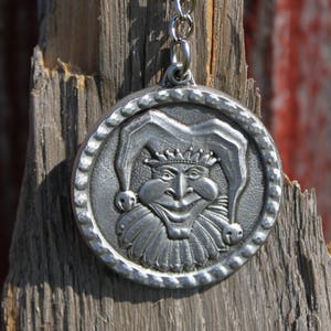 May include: A silver keychain with a round, detailed, pewter charm featuring a jester with a crown and a wide smile.