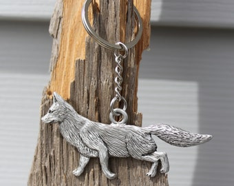 May include: A silver fox keychain with a detailed design. The fox is depicted in a running pose with its tail curled up. The keychain is attached to a silver chain and a silver ring.