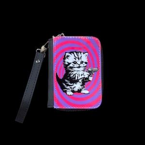 May include: A small wallet with a black wrist strap. The wallet features a graphic of a kitten holding a gun against a pink and purple spiral background. The wallet is black and has a zipper closure.