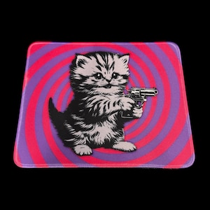 May include: Mousepad featuring a black and white kitten holding a gun. The mousepad has a pink and purple spiral design background. The kitten is the central focus of the image.