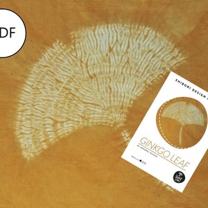 May include: A white Shibori design pattern for a Ginkgo Leaf, printed on a white sheet of paper. The pattern is a circle with a Ginkgo Leaf design inside. The text "Shibori Design Pattern" and "Ginkgo Leaf" are printed on the paper. The paper is on top of a brown fabric with a white Ginkgo Leaf design.