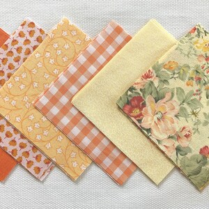 May include: Six fabric squares in various patterns, including floral, gingham, and geometric designs. The squares are in shades of yellow and orange.
