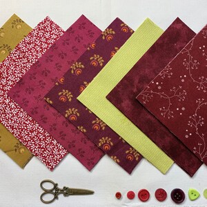 Op de afbeelding: Zes vierkante stukken stof in tinten rood, groen en geel met een wit bloemenpatroon. De vierkanten zijn in een verspringend patroon gerangschikt. Er zijn ook verschillende knopen in rood, groen en paars.