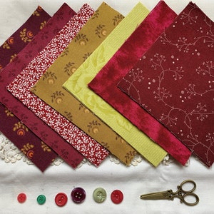 Puede incluir: Un conjunto de siete cuadrados de tela en tonos rojos y dorados con varios patrones. Los cuadrados están dispuestos en forma de abanico, con el cuadrado más grande en la parte superior y el más pequeño en la parte inferior. Hay seis botones de varios colores y un par de tijeras sobre una superficie blanca.
