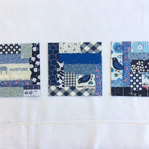 May include: Three blue and white patchwork fabric squares with different designs. The first square has a small elephant and the word "NURTURE" printed on it. The second square has a small bird and the words "moody blues" printed on it. The third square has a small bird and the words "blackbirds" printed on it.