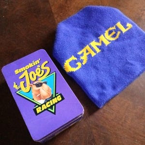 May include: A purple box with a camel cartoon character wearing sunglasses and the text "Smokin' Joe's Racing". A blue beanie with the word "Camel" in yellow letters.