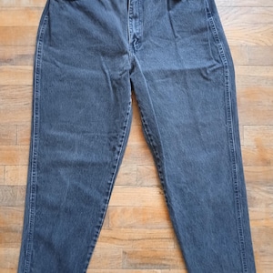 Może przedstawiać: Dżinsy z ciemnego denimu o prostym kroju nogawek. Dżinsy mają zapięcie na guziki i pięć kieszeni.