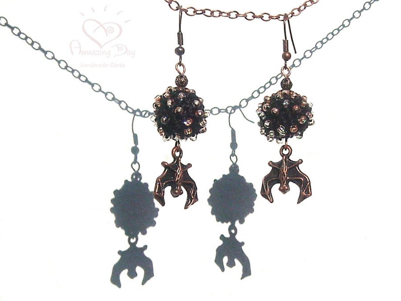 May include: A pair of earrings with black and silver bead clusters and dangling bat charms. The earrings are attached to a silver chain necklace.