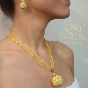 May include: A yellow beaded necklace with a matching pair of earrings. The necklace is made of a yellow ribbon and has a large yellow beaded pendant. The earrings are also made of yellow beads.
