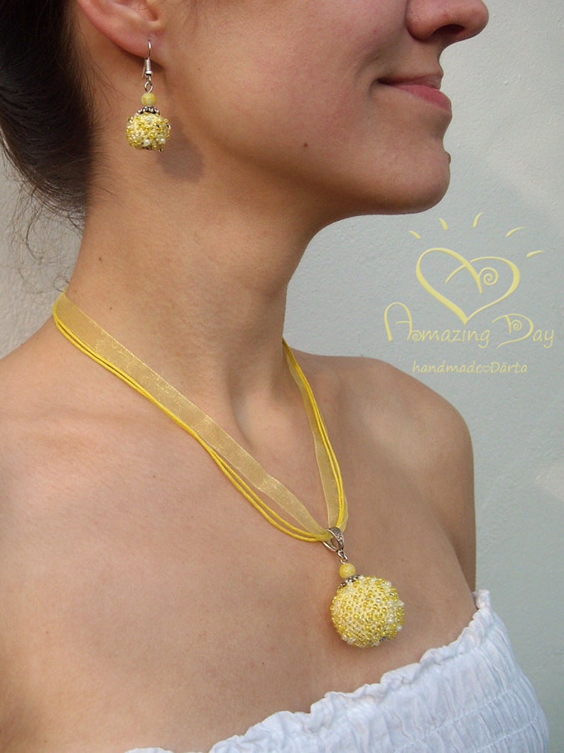 May include: A yellow beaded necklace with a matching pair of earrings. The necklace is made of a yellow ribbon and has a large yellow beaded pendant. The earrings are also made of yellow beads.