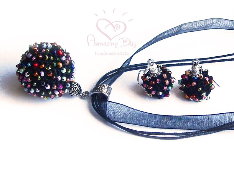 May include: A black beaded necklace and matching earrings with a multi-colored bead design. The necklace has a silver pendant and a black ribbon.