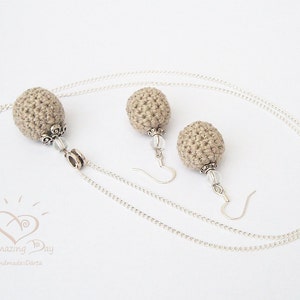 May include: A set of beige crocheted earrings and a necklace with silver chains and beads. The earrings and necklace feature a round, crocheted ball design.