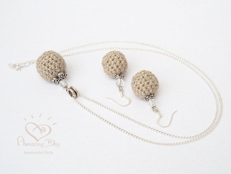 May include: A set of beige crocheted earrings and a necklace with silver chains and beads. The earrings and necklace feature a round, crocheted ball design.