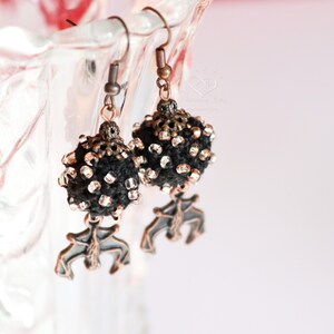 May include: A pair of black and silver beaded earrings with a copper-toned pendant in the shape of a stylized bird.