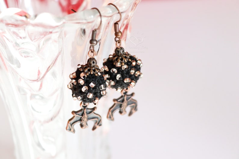 May include: A pair of black and silver beaded earrings with a copper-toned pendant in the shape of a stylized bird.
