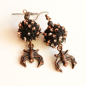 May include: A pair of black and copper earrings featuring a beaded sphere and a bat charm.