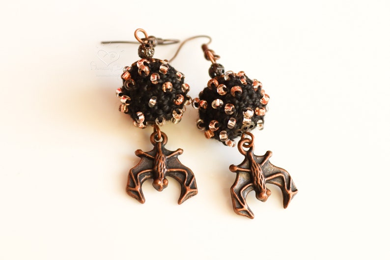May include: A pair of black and copper earrings featuring a beaded sphere and a bat charm.