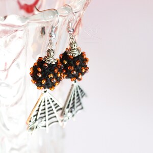 May include: Black and orange beaded earrings with a silver spiderweb dangle.