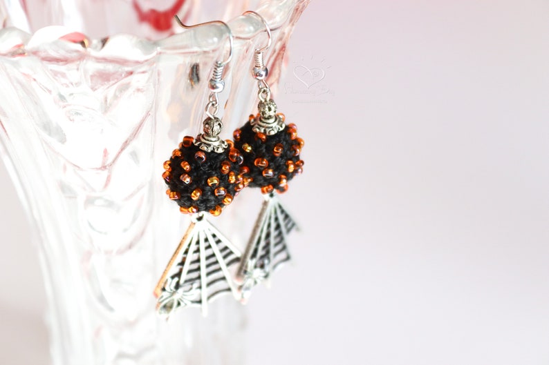 May include: Black and orange beaded earrings with a silver spiderweb dangle.