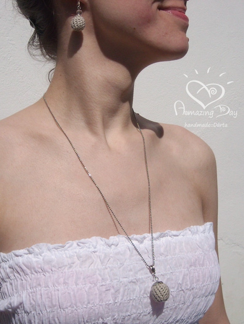 May include: A woman wearing a white strapless top with a silver chain necklace and a crocheted pendant. She is also wearing a pair of crocheted earrings. The necklace and earrings are both beige in color.
