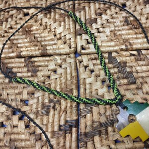May include: A black and green cord necklace with a green, yellow, and white puzzle piece pendant.