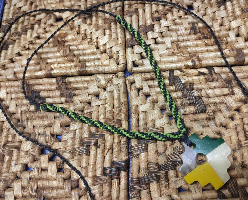 May include: A black and green cord necklace with a green, yellow, and white puzzle piece pendant.