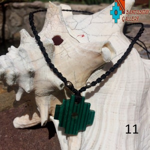 May include: A green jade cross pendant on a black cord necklace with silver beads. The necklace is displayed on a white seashell. The number 11 is visible in the bottom right corner of the image.