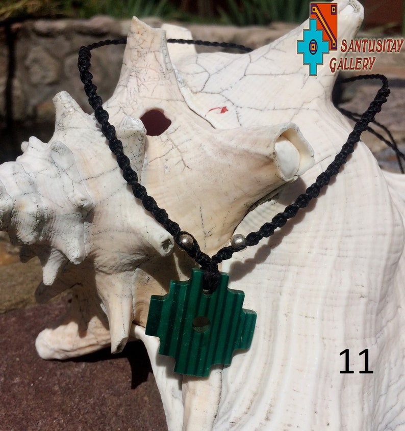 May include: A green jade cross pendant on a black cord necklace with silver beads. The necklace is displayed on a white seashell. The number 11 is visible in the bottom right corner of the image.