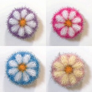 May include: Four crocheted flower-shaped dishcloths in different colors: purple, pink, blue, and yellow. Each dishcloth has a white daisy design in the center.