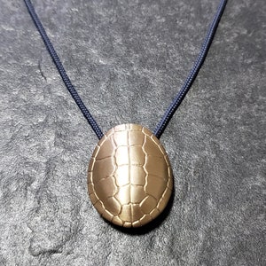 May include: A gold-colored turtle shell pendant on a dark blue cord necklace.