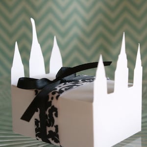 May include: White cardboard box shaped like a church with black and white ribbon tied around it.