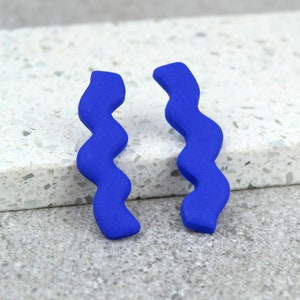 Könnte beinhalten: Ein Paar blaue, wellenförmige Ohrringe. Die Ohrringe sind aus einem glatten, matten Material gefertigt.