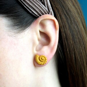 May include: A pair of yellow shell-shaped earrings. The earrings are small and delicate, and they are a great way to add a touch of whimsy to any outfit.