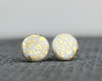 May include: A pair of white round stud earrings with a gold flecked pattern.