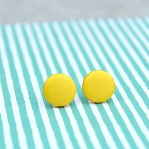 May include: A pair of yellow round stud earrings. The earrings are on a striped background.