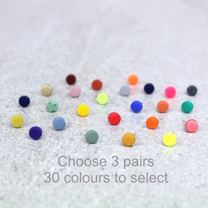May include: Thirty colourful round stud earrings, arranged in a semi-circle on a grey textured surface. Choose 3 pairs.