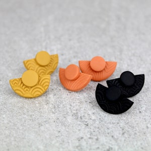 May include: Three pairs of half-circle earrings with a textured pattern. The earrings are in black, orange, and yellow.