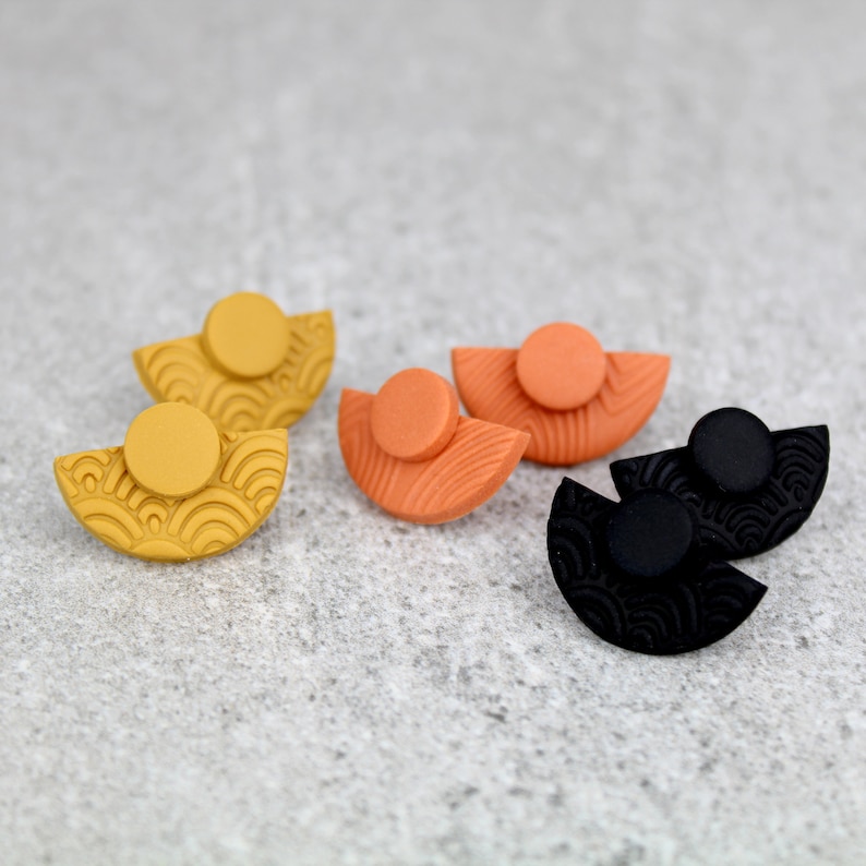 May include: Three pairs of half-circle earrings with a textured pattern. The earrings are in black, orange, and yellow.
