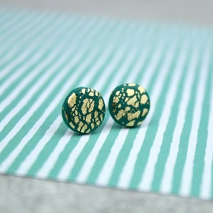 May include: A pair of round green earrings with gold flecks. The earrings are on a striped green and white background.