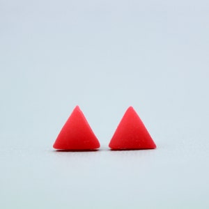 Peut inclure: Deux petites boucles d'oreilles de forme triangulaire de couleur rouge vif.