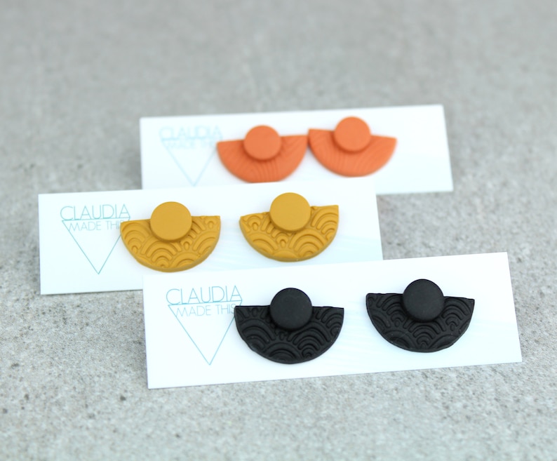 May include: Three pairs of earrings with a half-circle design and a textured pattern. The earrings are in black, orange, and yellow.