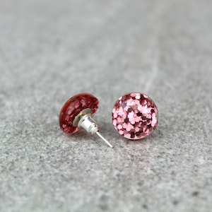 May include: A pair of pink glitter stud earrings. The earrings are round and have a silver post.