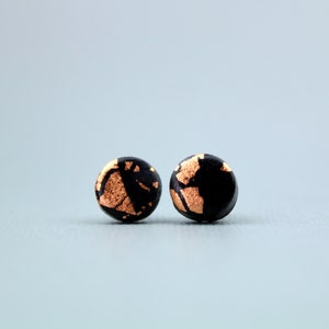 May include: A pair of black and gold round stud earrings. The earrings have a gold foil design on a black background.