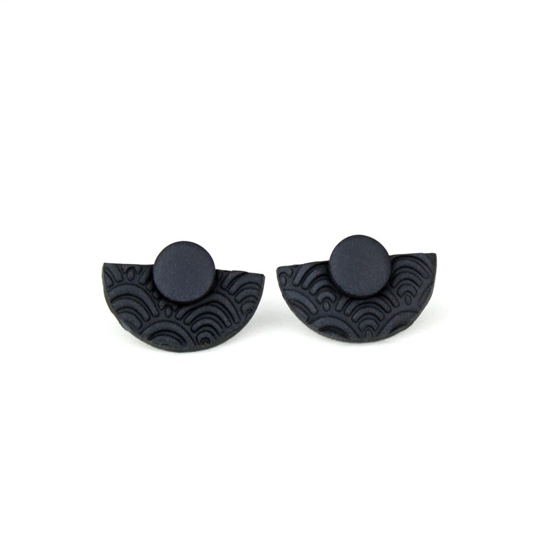 May include: A pair of black stud earrings with a half-circle design and a textured pattern. The earrings are made of polymer clay.