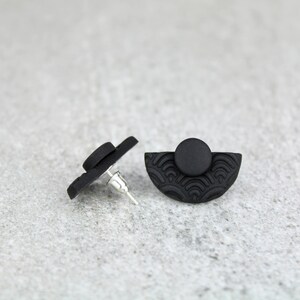 May include: A pair of black stud earrings with a half-circle design and a textured pattern. The earrings are made of polymer clay.