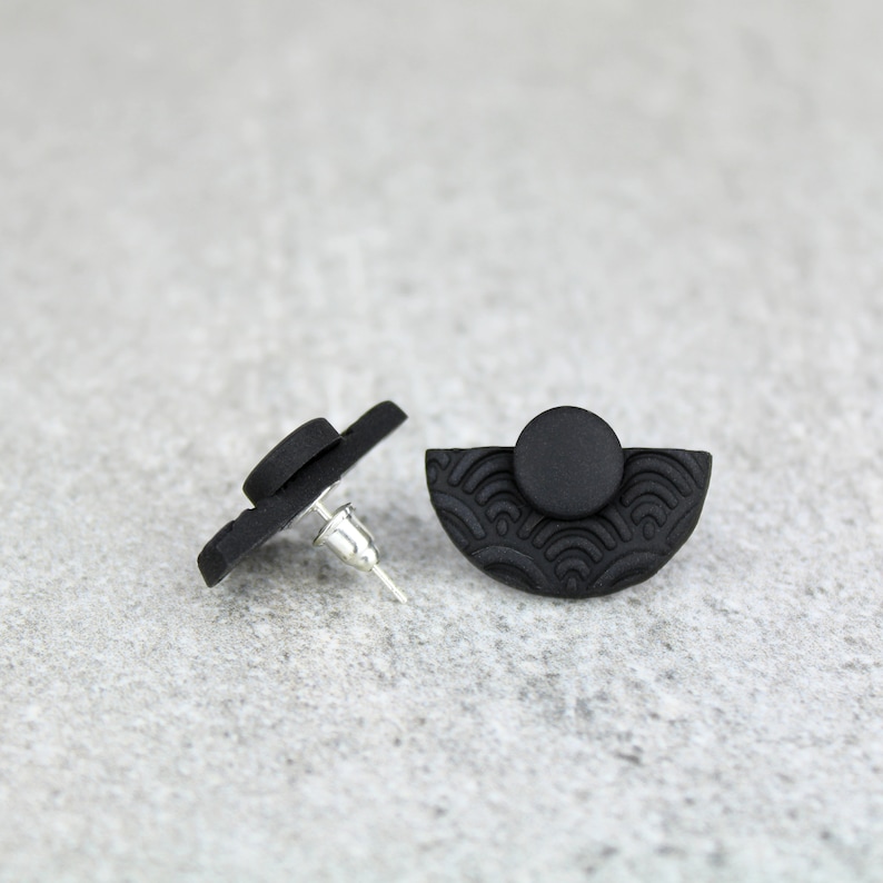 May include: A pair of black stud earrings with a half-circle design and a textured pattern. The earrings are made of polymer clay.