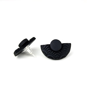 May include: A pair of black stud earrings with a half-circle design and a textured wave pattern. The earrings are made of polymer clay and have silver posts.