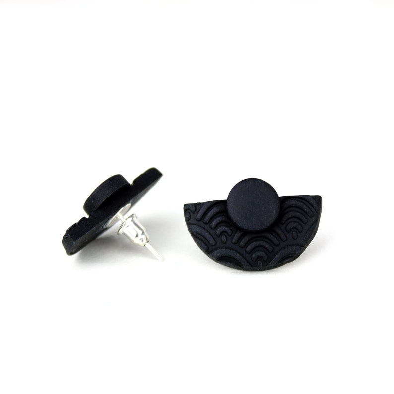 May include: A pair of black stud earrings with a half-circle design and a textured wave pattern. The earrings are made of polymer clay and have silver posts.