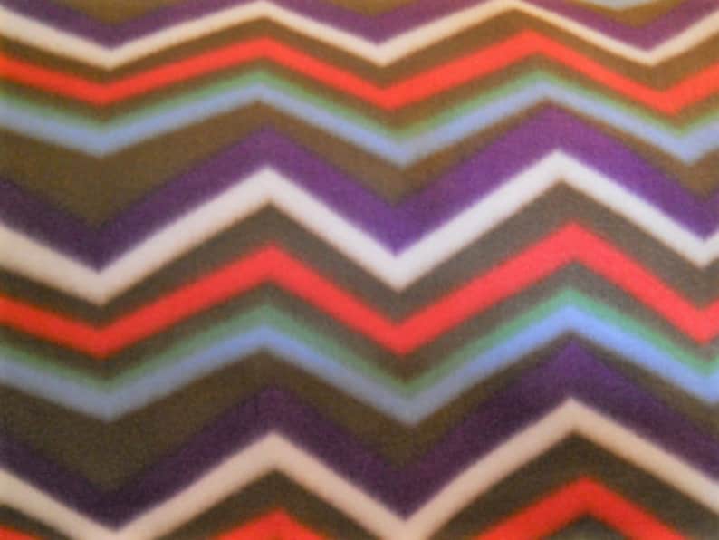 May include: A colorful chevron pattern in shades of red, white, purple, blue, green, and brown. The zig-zag design is a repeating pattern across the fabric. The fabric has a soft, fuzzy texture.