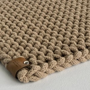 May include: A beige knitted trivet with a brown leather tag that says "Handmade with Love".